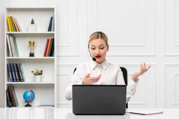 Servizio clienti donna carina in camicia bianca con auricolare e computer che parla e agita le mani