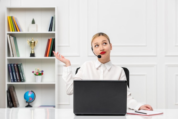 Servizio clienti donna carina in camicia bianca con auricolare e computer guardando in alto e pensando