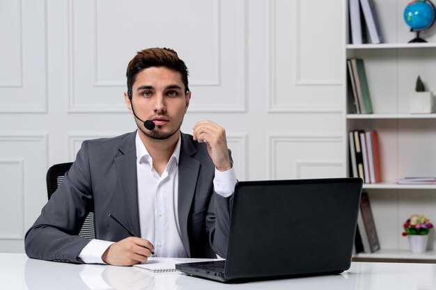 Servizio clienti grazioso gentiluomo con computer in abito da ufficio grigio che sembra serio