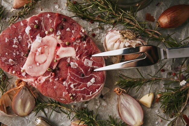 Servizio da tavola, cipolle, romero, bistecca di carne cruda, sale, pepe, aglio, olio d'oliva, forchetta. primo piano, vista dall'alto