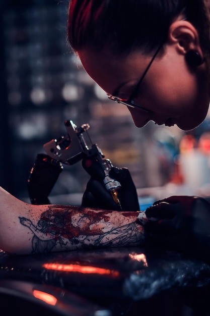 Servizio fotografico del primo piano della realizzazione del tatuaggio, l'artista sta lavorando con la macchina del tatuaggio sulla mano del cliente.