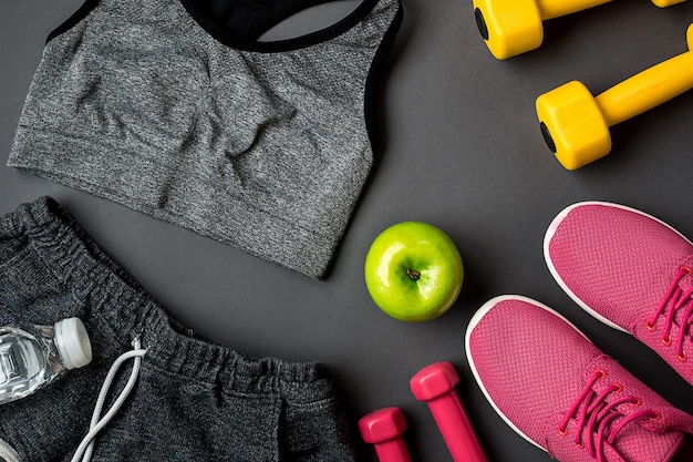 Set da atleta con abbigliamento femminile, scarpe da ginnastica e bottiglia d'acqua su sfondo grigio