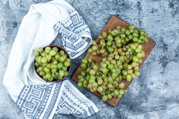 Set di asciugatutto e uva verde in una ciotola su intonaco grungy e sfondo tagliere laici piatta.