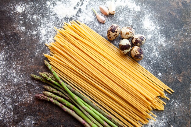 Set di asparagi, uova e aglio e spaghetti su uno sfondo scuro con texture. vista dall'alto.