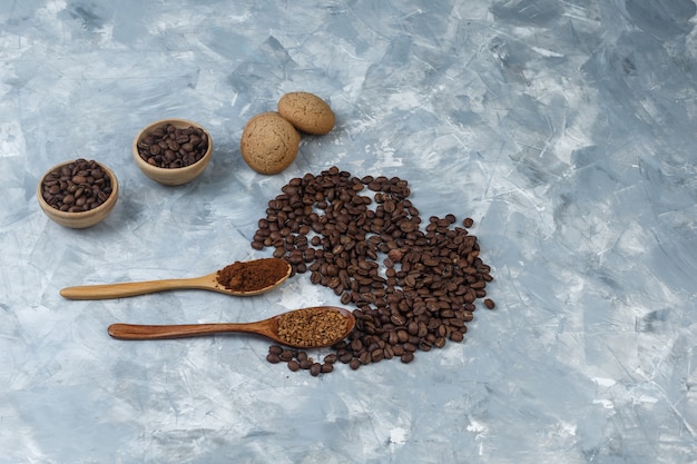 Set di biscotti, caffè istantaneo e farina di caffè in cucchiai di legno e chicchi di caffè in ciotole su uno sfondo di marmo azzurro. avvicinamento.