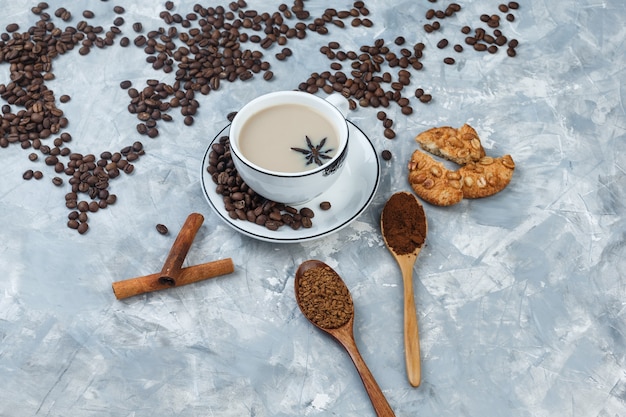 Set di biscotti, chicchi di caffè, caffè macinato, bastoncini di cannella e caffè in una tazza su uno sfondo di gesso grigio. vista ad alto angolo.