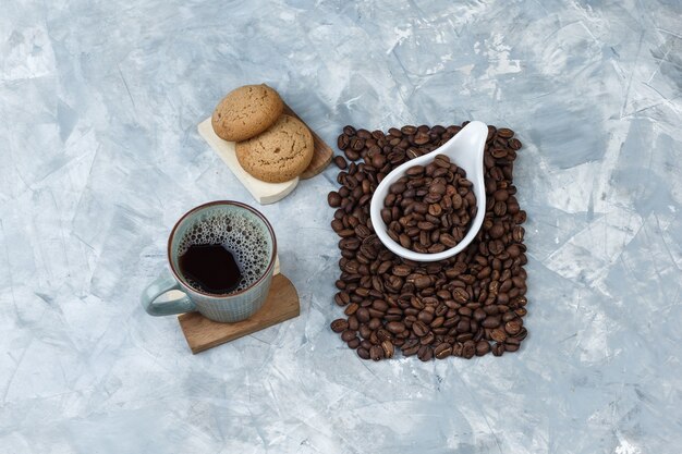 Set di biscotti su un tagliere, una tazza di caffè e chicchi di caffè in una brocca di porcellana bianca