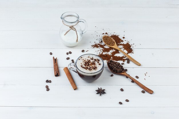 Set di caffè macinato, chicchi di caffè, bastoncini di cannella, latte e caffè in una tazza su uno sfondo di legno. vista ad alto angolo.