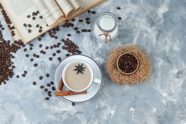 Set di chicchi di caffè, libro, latte, spezie e caffè in una tazza su uno sfondo di gesso grigio. vista dall'alto.