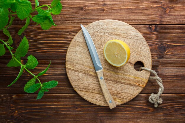 Set di foglie, coltello di legno, tagliere e mezzo limone su una superficie di legno. vista dall'alto. copia spazio per il testo