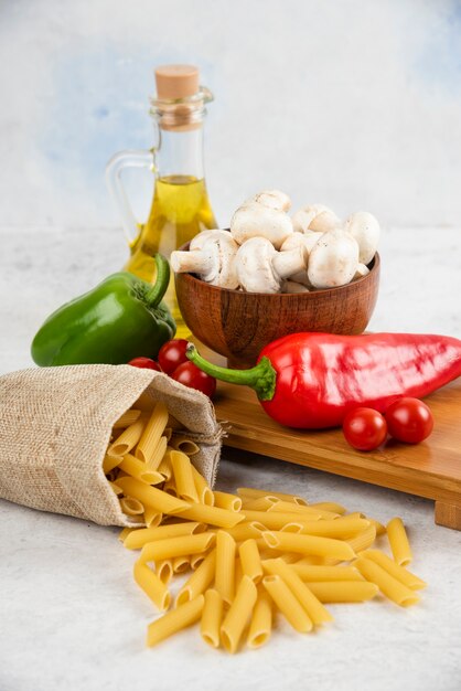 Set di funghi, olio extra vergine di oliva, pasta, pomodorini e peperoncino su un pezzo di marmo.