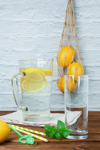 Set di limoni, foglie e caraffa di limone su un panno bianco su una superficie di legno e bianca. vista laterale.