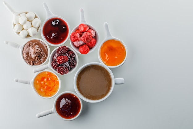 Set di marmellate, lamponi, zucchero, cioccolato in tazze e una tazza di caffè su uno spazio bianco superficiale per il testo