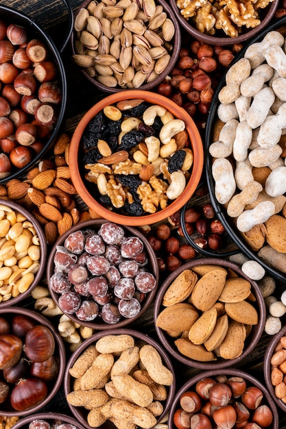 Set di noci pecan, pistacchi, mandorle, arachidi, anacardi, pinoli e noci assortite e frutta secca in mini ciotole diverse e padella nera. vista dall'alto.