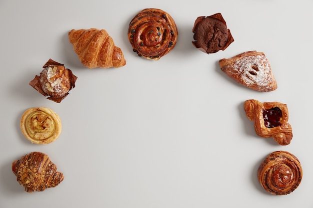 Set di prodotti alimentari da forno. Grande varietà di deliziosi dolci a semicerchio su sfondo bianco. Croissant, muffin, turbinii e panini da mangiare. Buonissimo dessert. Cibo dolce e alimentazione malsana