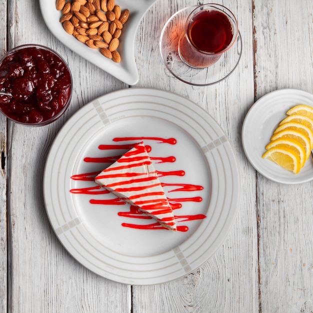 Set di tè, noci, marmellata di frutta, fette di limoni e deliziosi dessert in un piatto su un fondo di legno bianco. vista dall'alto.