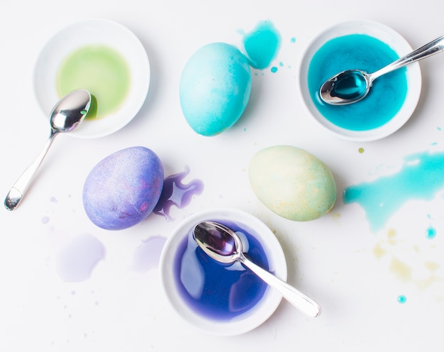 Set di uova di Pasqua colorate tra macchie, cucchiai e liquido di tintura in piattini