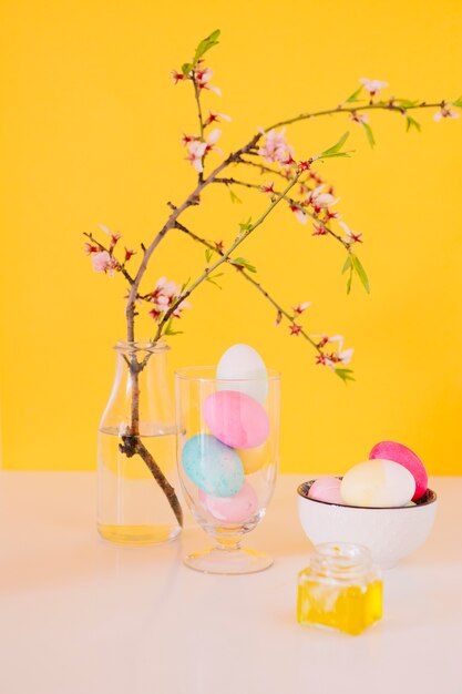 Set di uova di Pasqua luminose vicino fiore ramoscello in vaso con acqua e liquido di tintura