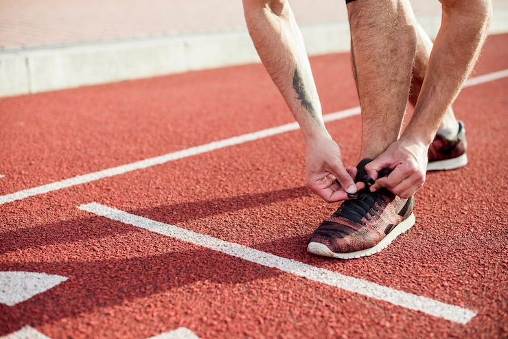 Foto gratuito sezione bassa dell'atleta maschio sulla linea di partenza legando il laccio sulla pista da corsa