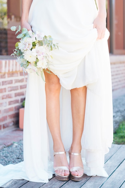 Sezione bassa di un bouquet di fiori della holding della sposa in mano mostrando i suoi tacchi alti alla moda