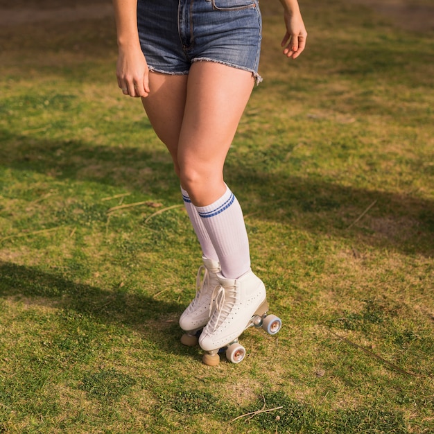 Sezione bassa di una giovane donna con roller skate in piedi sull&#39;erba verde