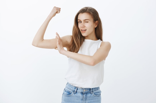 Sfacciata ragazza attraente allenamento in palestra, flettendo i bicipiti e ammiccando, invitando a comprare l'iscrizione, unirsi alla squadra di fitness