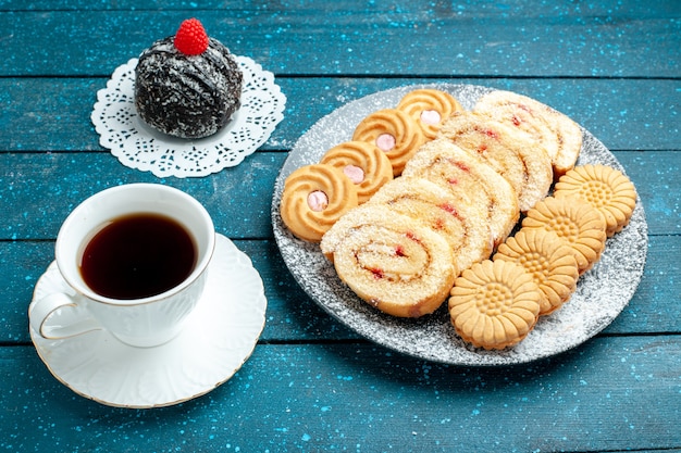 Sfera squisita del cioccolato di vista frontale con la tazza dei rotoli di tè e dei biscotti sul biscotto del biscotto della torta dolce del tè rustico blu della scrivania