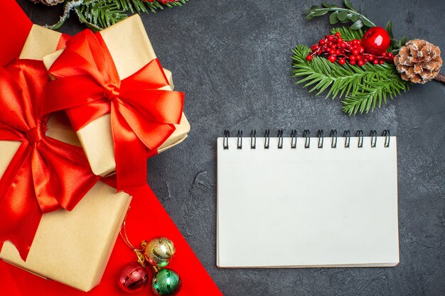 Sfondo di Natale con bellissimi doni con nastro a forma di fiocco e accessori per la decorazione di rami di abete notebook su un tavolo scuro
