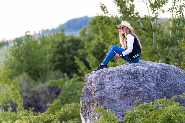 Shallow focus shot di una donna europea con cappello da cowboy seduto su una roccia in natura