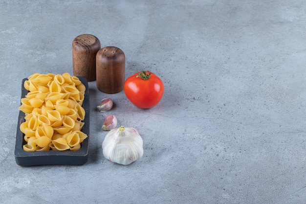 Shell pasta cruda in una tavola con pomodoro rosso fresco e aglio.