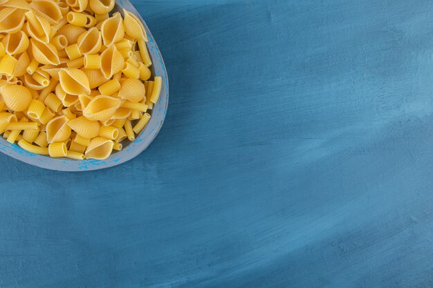 Shell pasta cruda in una tavola su uno sfondo blu scuro.