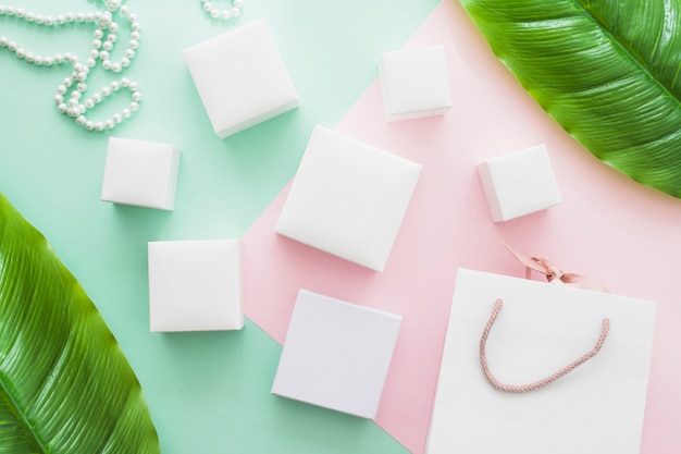 Shopping bag, collana di perle e diversi tipi di scatole bianche su sfondo di carta pastello