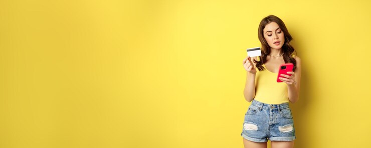 Foto gratuito shopping online donna bruna elegante con smartphone e carta di credito che paga in app usando un'applicazione per telefono cellulare che compra smth in piedi su uno sfondo giallo