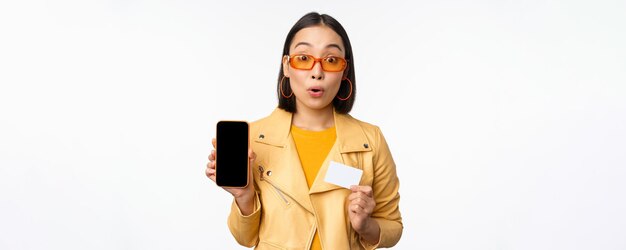 Shopping online e concetto di persone donna asiatica alla moda che mostra lo schermo del telefono cellulare e la carta di credito s