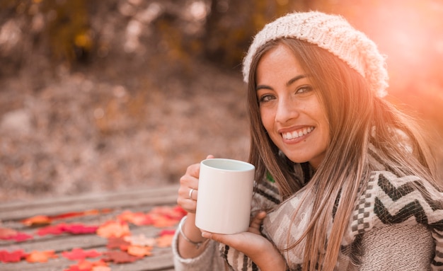 Signora affascinante con la tazza nella sosta di autunno