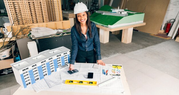 Signora afroamericana felice in casco di sicurezza che sta vicino al modello di costruzione