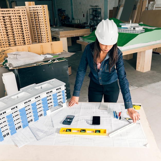 Signora afroamericana in casco di sicurezza che sta vicino al modello di costruzione