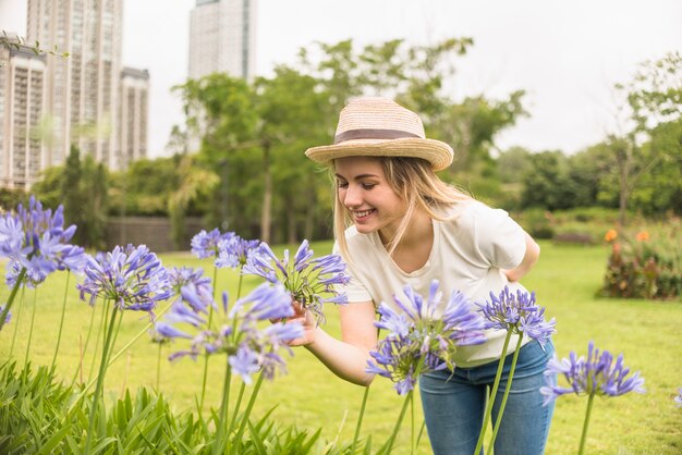 Signora allegra in cappello che tiene le fioriture blu nel parco della città