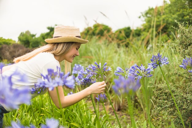 Signora allegra in cappello vicino alle fioriture blu nel parco