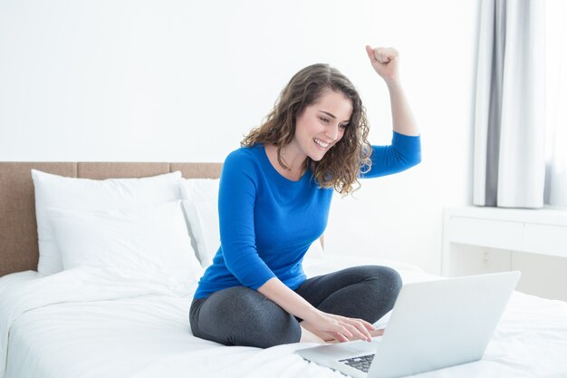 Signora allegra lavorando al computer portatile e seduto sul letto