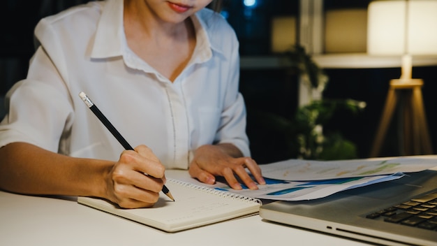 Signora asiatica indipendente che utilizza il duro lavoro del computer portatile nel soggiorno di casa.