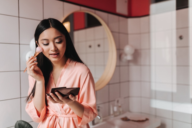 Foto gratuito signora attraente in abito rosa mette la polvere sul viso, posa in bagno