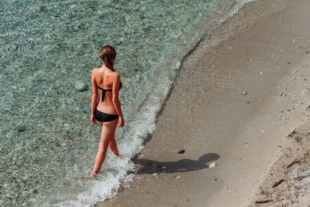 Signora attraente in bikini a fascia che cammina nel mare durante il giorno.