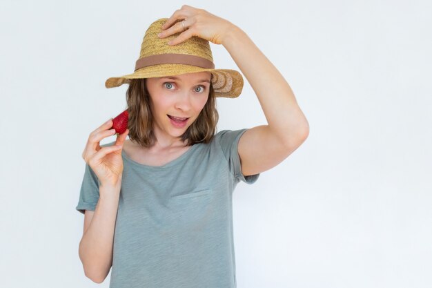 Signora attraente in cappello che tiene fragola e saluto maturi