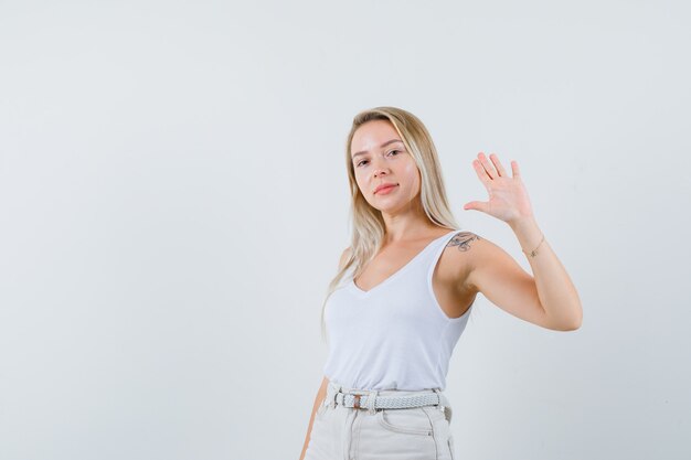 Signora bionda agitando la mano per dire addio in singoletto, pantaloni e guardando fiducioso