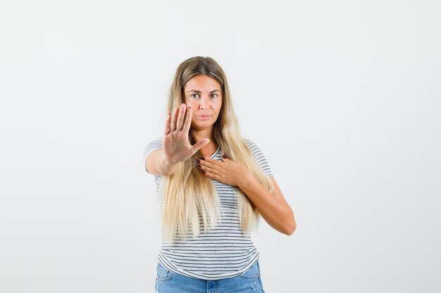 Signora bionda alzando la mano in modo rifiutante in maglietta e guardando seria. vista frontale.