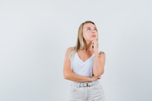 Signora bionda appoggiando il mento a portata di mano in canottiera, pantaloni e guardando pensieroso