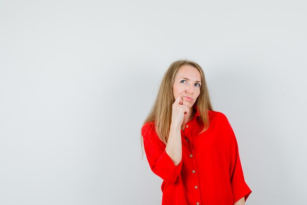 Signora bionda appoggiando il mento sul pugno in camicia rossa e guardando esitante,