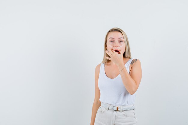 Signora bionda che cerca di forzare un sorriso sul viso in canottiera, vista frontale dei pantaloni.