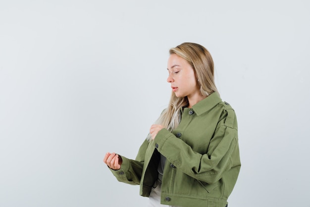 Signora bionda che finge di tenere qualcosa in giacca, pantaloni e sguardo concentrato, vista frontale.